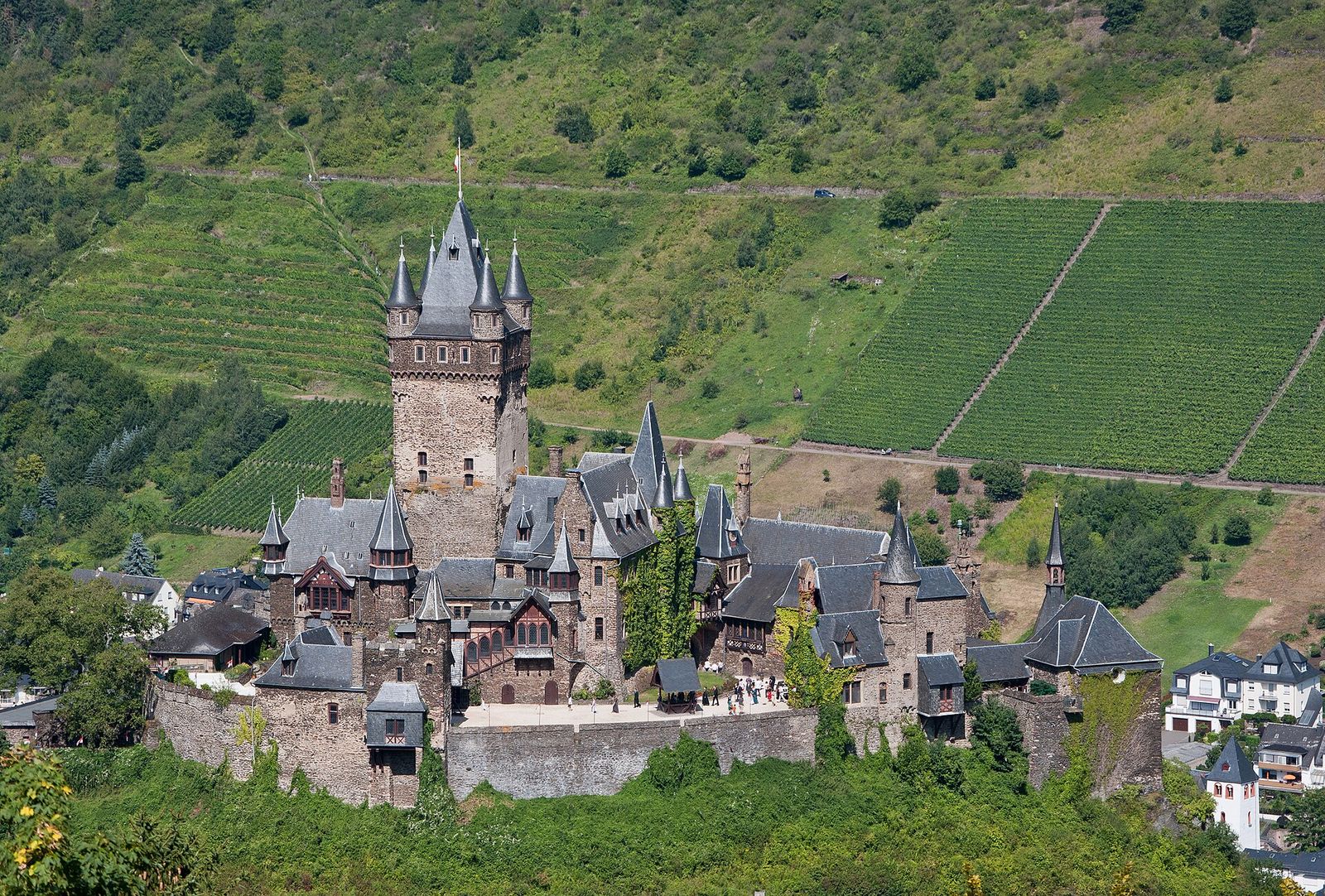 Die Reichsburg Cochem mit Bergfried und spitzen Türmchen, im Hintergrund steile Weinbergterrassen