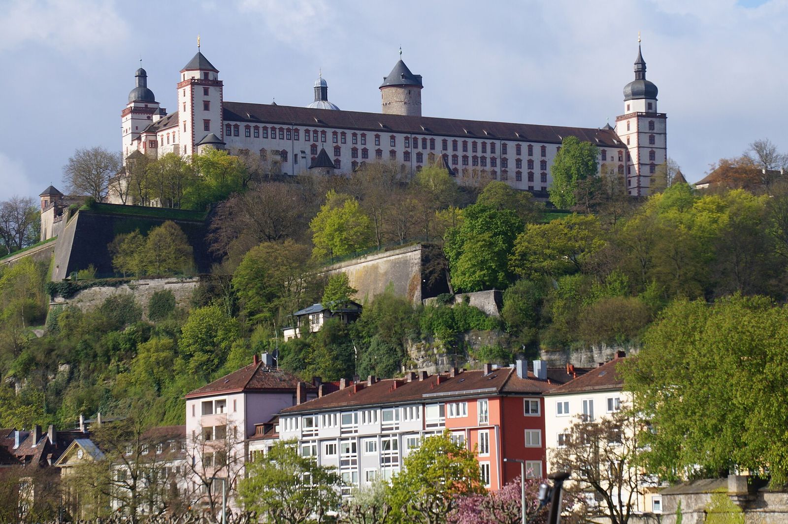 Die Festung Marienberg mit ihren Türmen auf dem grünen Hang über den Häusern am Mainufer in Würzburg